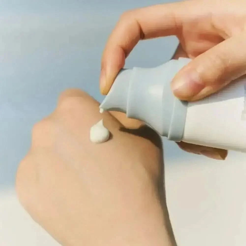 Un produit de soin dans une boîte aux motifs ondulés et un tube blanc étiqueté « Sérum solaire Madagascar Centella » de Jay Cosmetic offre une hydratation intense et une protection SPF 50. Une petite plante est présente à gauche sur un fond neutre et minimaliste.