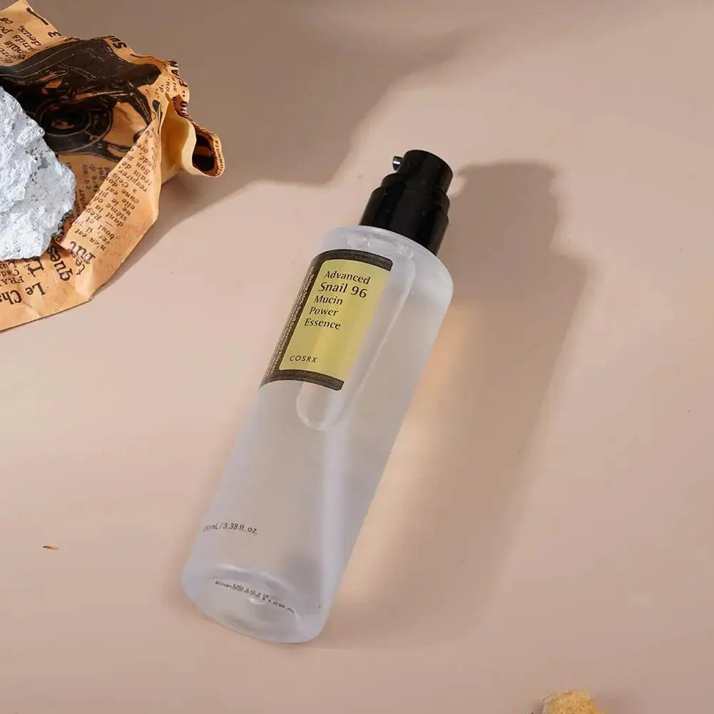 Deux produits de soin de la gamme COSRX de Jay Cosmetic, Essence Ensemble escargot, sont présentés sur un fond blanc : un flacon hydratant dAdvanced Snail 96 Mucin Power Essence et un pot dAdvanced Snail 92 All in One Cream avec un signe plus entre eux, idéal pour réparer la peau.