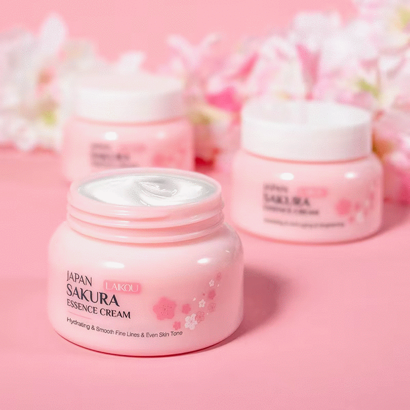 Lensemble de soins du visage Laikou Sakura de Jay Cosmetic est présenté sur une surface rose avec son Nettoyant Visage Sakura, son toner, sa crème, son sérum à la niacinamide et son baume à lèvres dans un emballage sur le thème des fleurs de cerisier. Une boîte ouverte révélant un motif floral se trouve au milieu de pétales de fleurs de cerisier dispersés.
