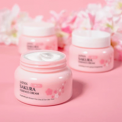 Lensemble de soins du visage Laikou Sakura de Jay Cosmetic est présenté sur une surface rose avec son Nettoyant Visage Sakura, son toner, sa crème, son sérum à la niacinamide et son baume à lèvres dans un emballage sur le thème des fleurs de cerisier. Une boîte ouverte révélant un motif floral se trouve au milieu de pétales de fleurs de cerisier dispersés.